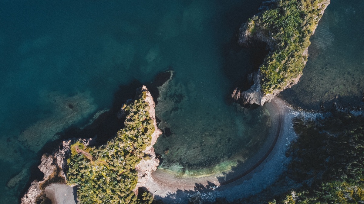 Breathtaking aerial photo of a lush island coastline with clear blue water and a curved shore