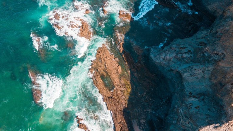 A captivating aerial shot showcasing rugged coastal rock formations and vibrant turquoise waves