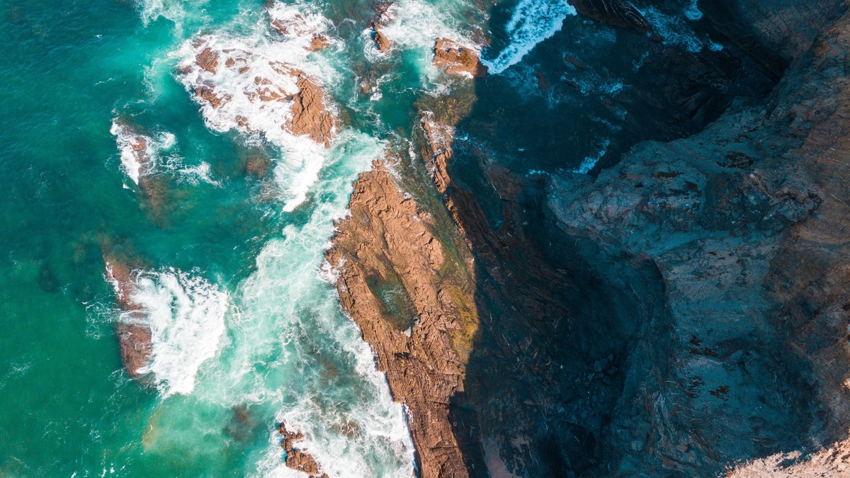 A captivating aerial shot showcasing rugged coastal rock formations and vibrant turquoise waves