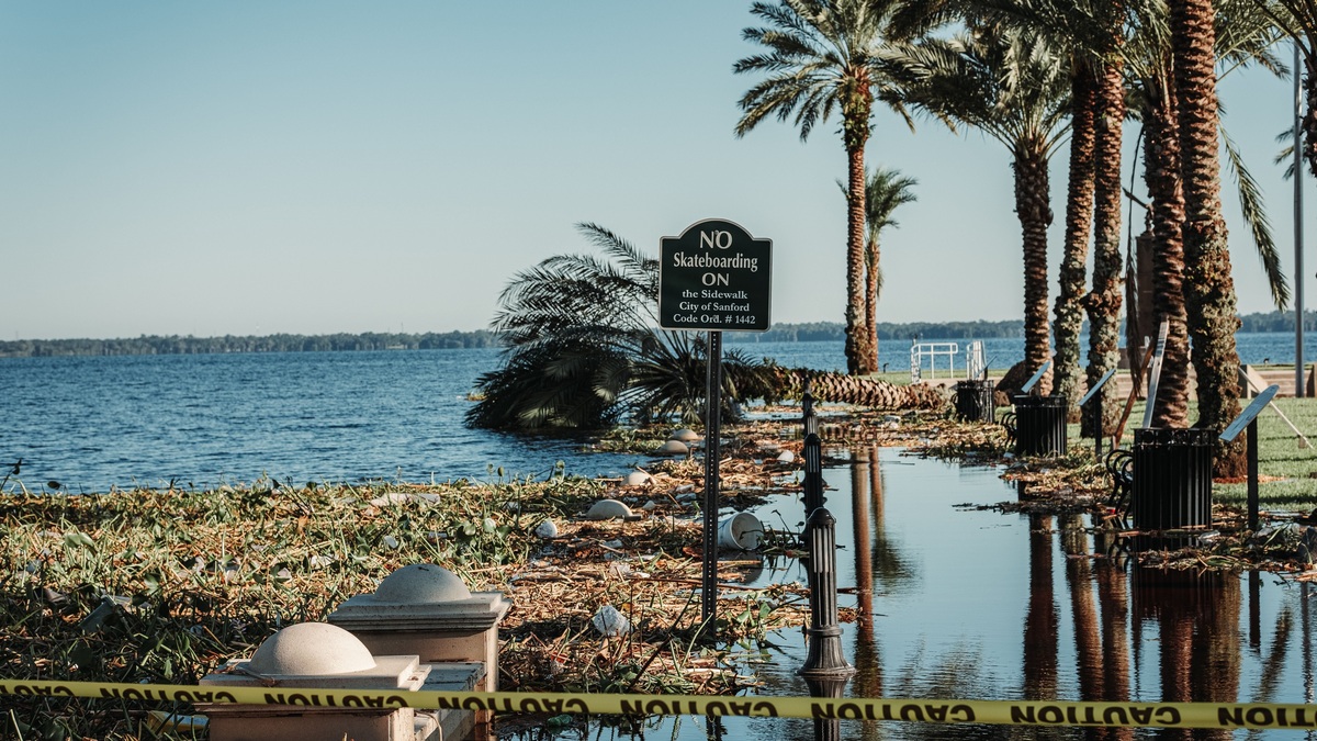 A flooded pathway with caution tape and palm trees by a lake in Sanford, Florida