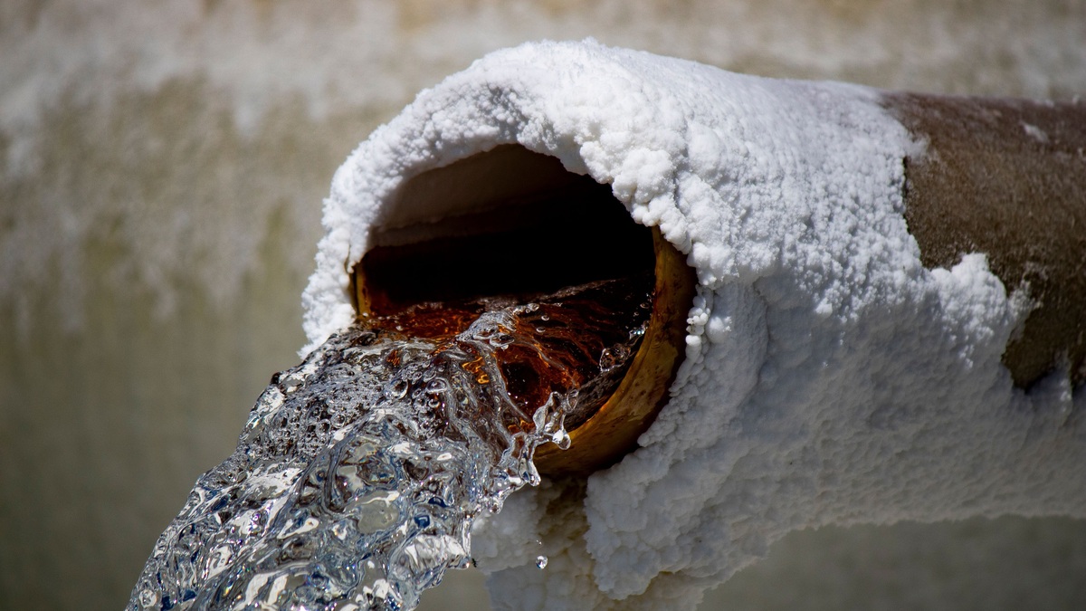 Close-up of water flowing from a rusty pipe with salt deposits, capturing motion and texture