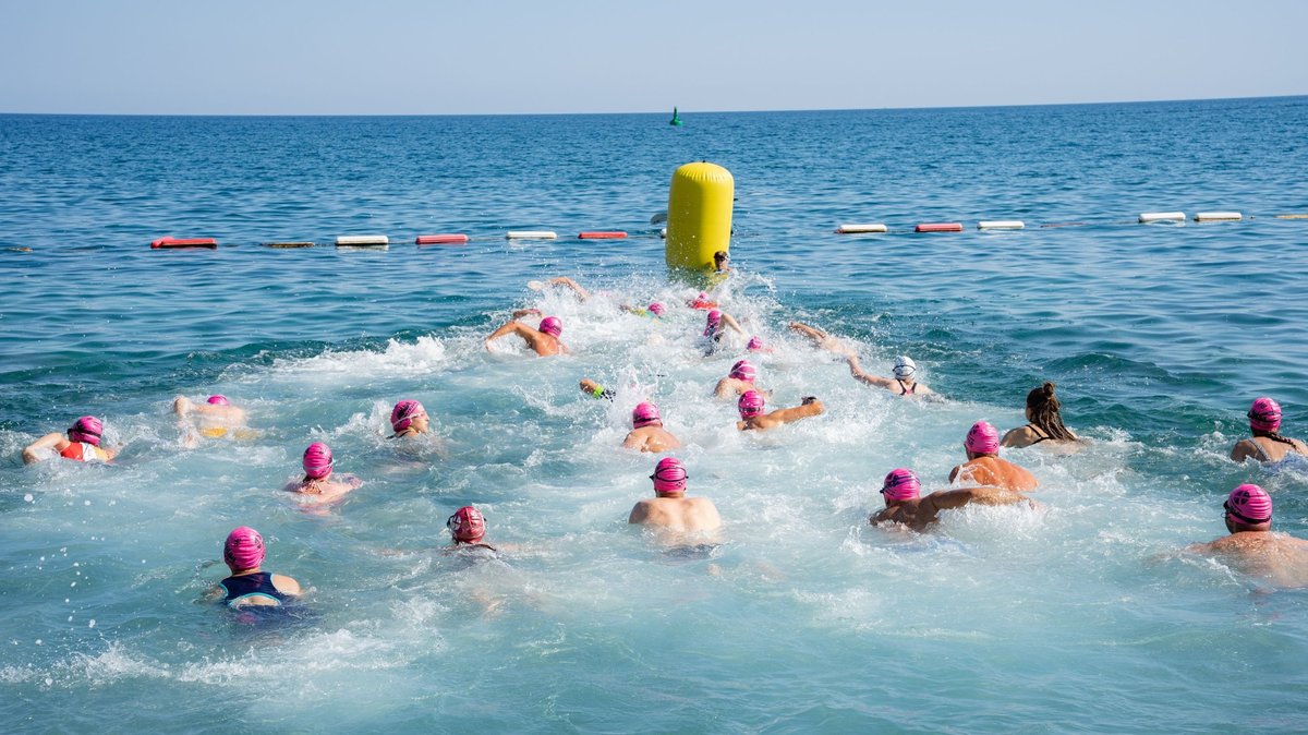 Open-water swimmers in bright caps racing toward a buoy at sea