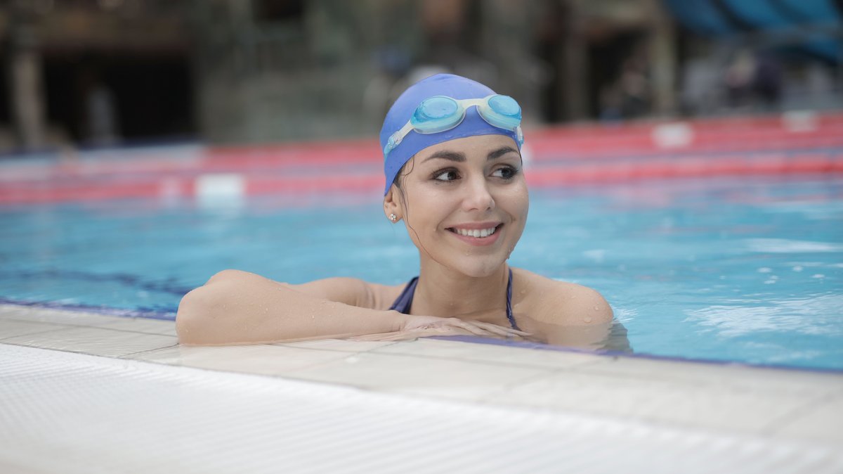 A smiling swimmer wearing a cap and goggles in a pool