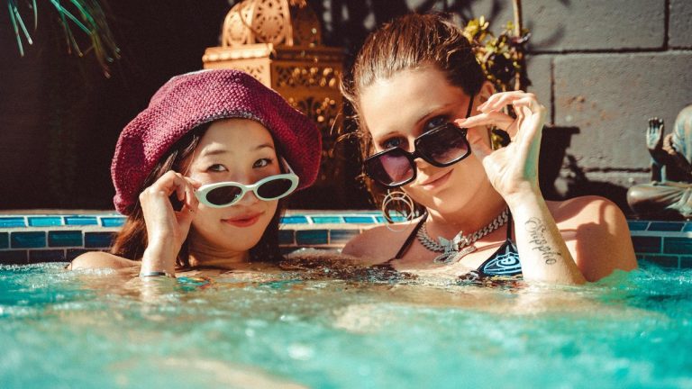 Two fashionable women enjoy a sunny day in an outdoor hot tub, exuding summer vibes and fun