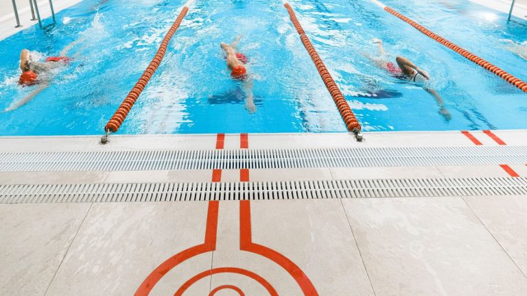 Three athletes swimming freestyle in a bright indoor pool