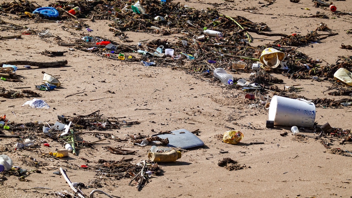 Plastic waste and debris littered across a sandy beach shore