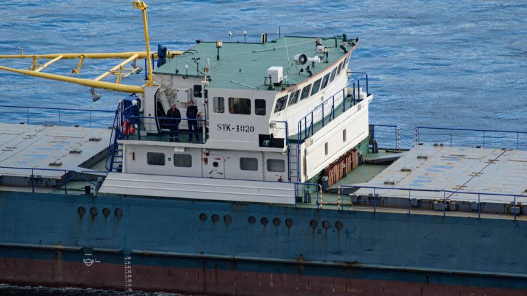 Close-up view of cargo ship with crew at the helm, navigating open blue waters