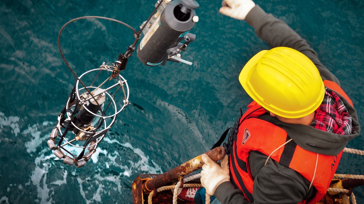 Worker in hard hat and life vest operates machinery on an offshore platform above ocean waters