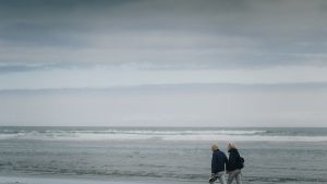 Two senior adults walking on a gloomy beach, offering a sense of serenity and reflection