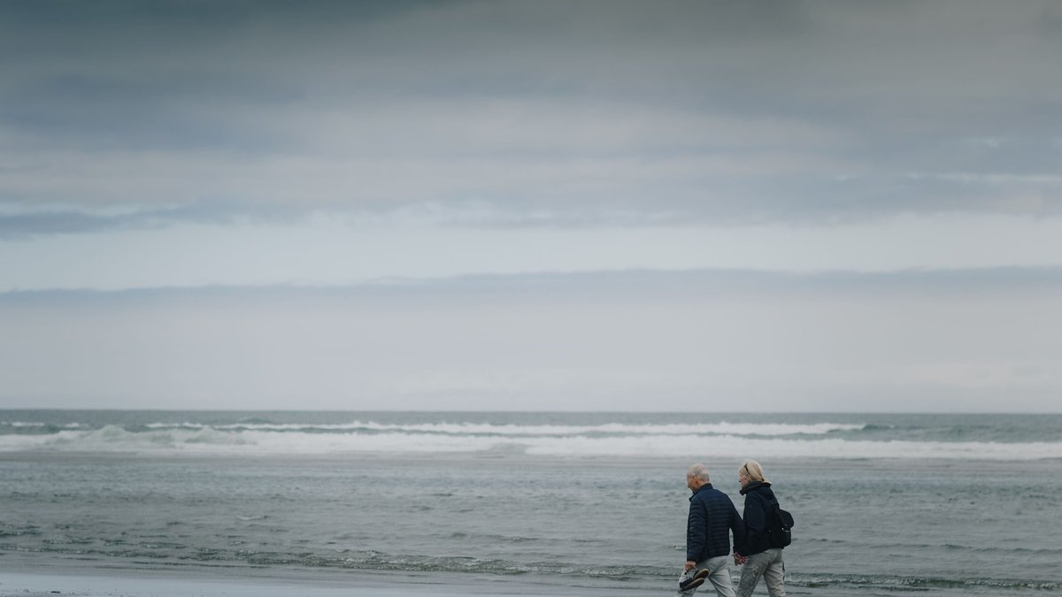 Two senior adults walking on a gloomy beach, offering a sense of serenity and reflection