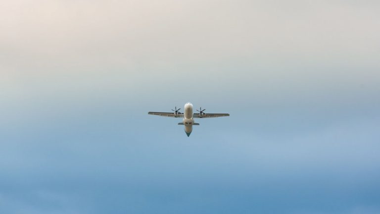 A propeller airplane mid-flight against a clear blue sky, captured from below