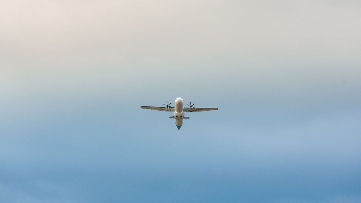 A propeller airplane mid-flight against a clear blue sky, captured from below