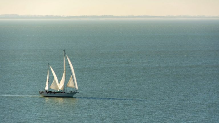 Peaceful scene of a large sailing ship with white sails on a tranquil sea during the day