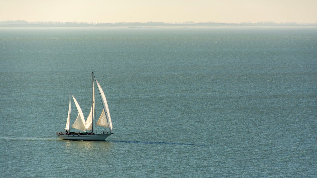 Peaceful scene of a large sailing ship with white sails on a tranquil sea during the day
