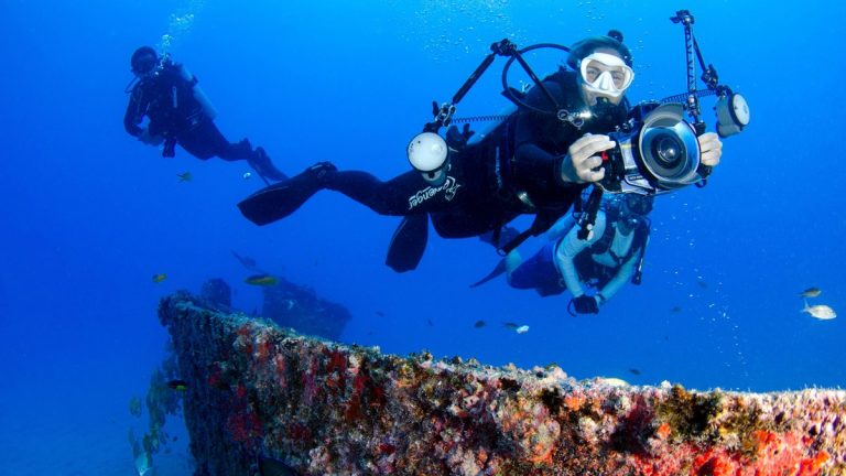 Two scuba divers capturing the vibrant marine life near an underwater wreck in crystal clear waters