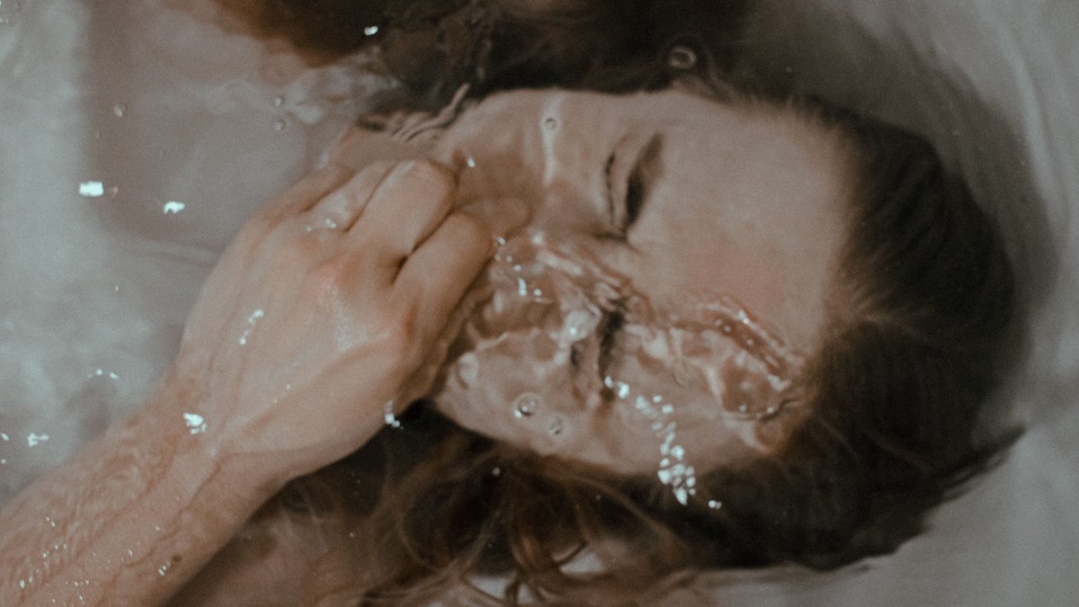 Top view of frowning teen female holding nose and keeping breath lying in bathtub