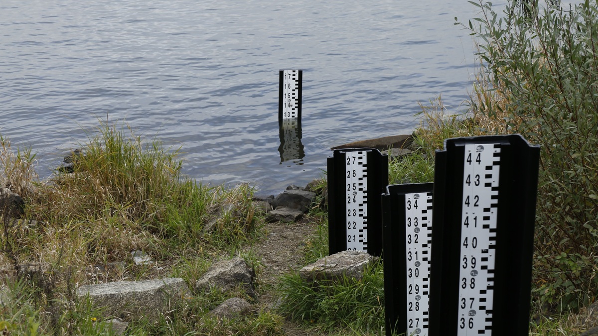 A water level measurement post standing in a lake, surrounded by rocks and vegetation