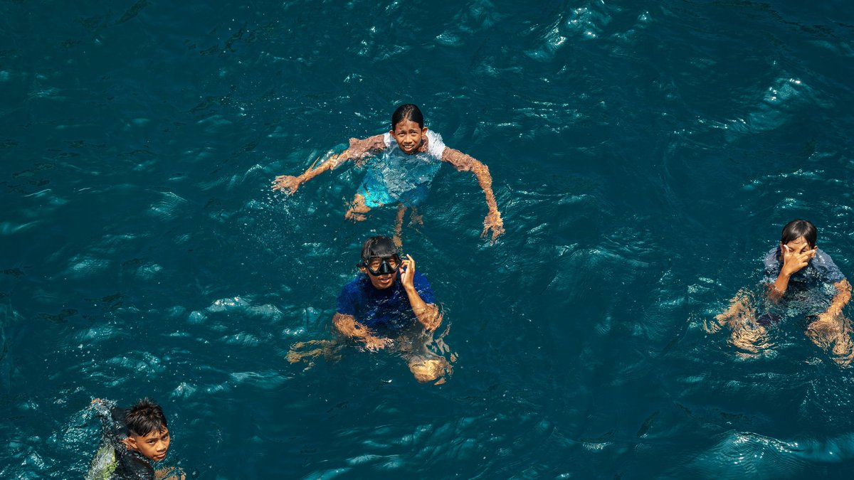 Aerial view of four children joyfully swimming in clear blue water on a sunny day