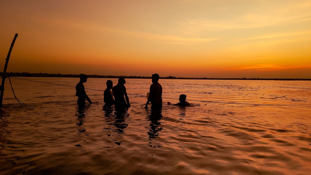 Silhouetted teenagers swimming together in a lake during a vibrant sunset, creating a joyful summer scene