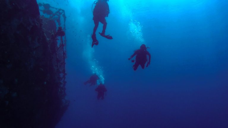 A group of aquanauts diving together near an underwater structure