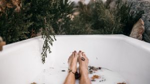 Feet soaking in an outdoor bathtub with floating flowers and greenery for relaxation