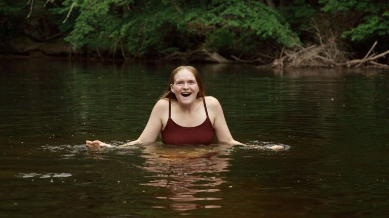 A woman swimming in a quiet lake surrounded by green vegetation