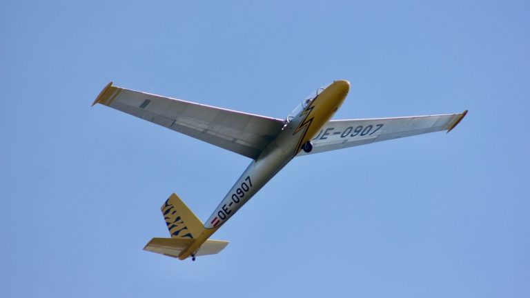 A sleek glider aircraft OE-0907 soaring gracefully against a clear blue sky