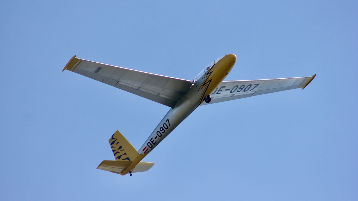 A sleek glider aircraft OE-0907 soaring gracefully against a clear blue sky