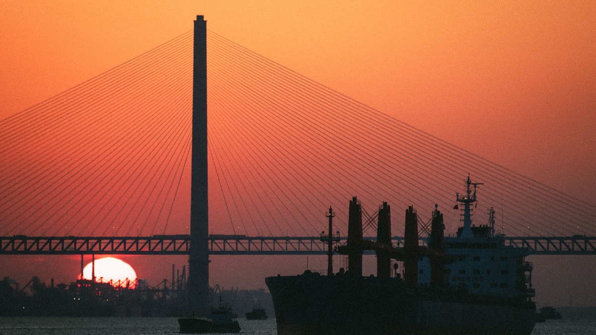 A cargo ship passing beneath a suspension bridge at sunset