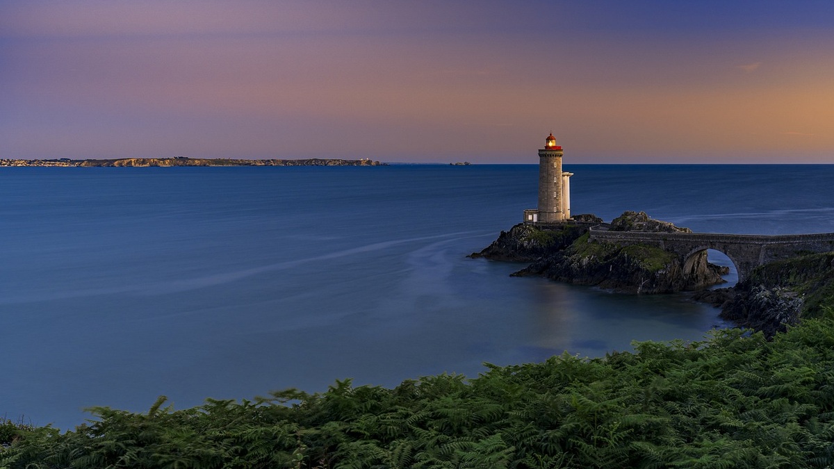 A lighthouse on a rocky coast at sunset