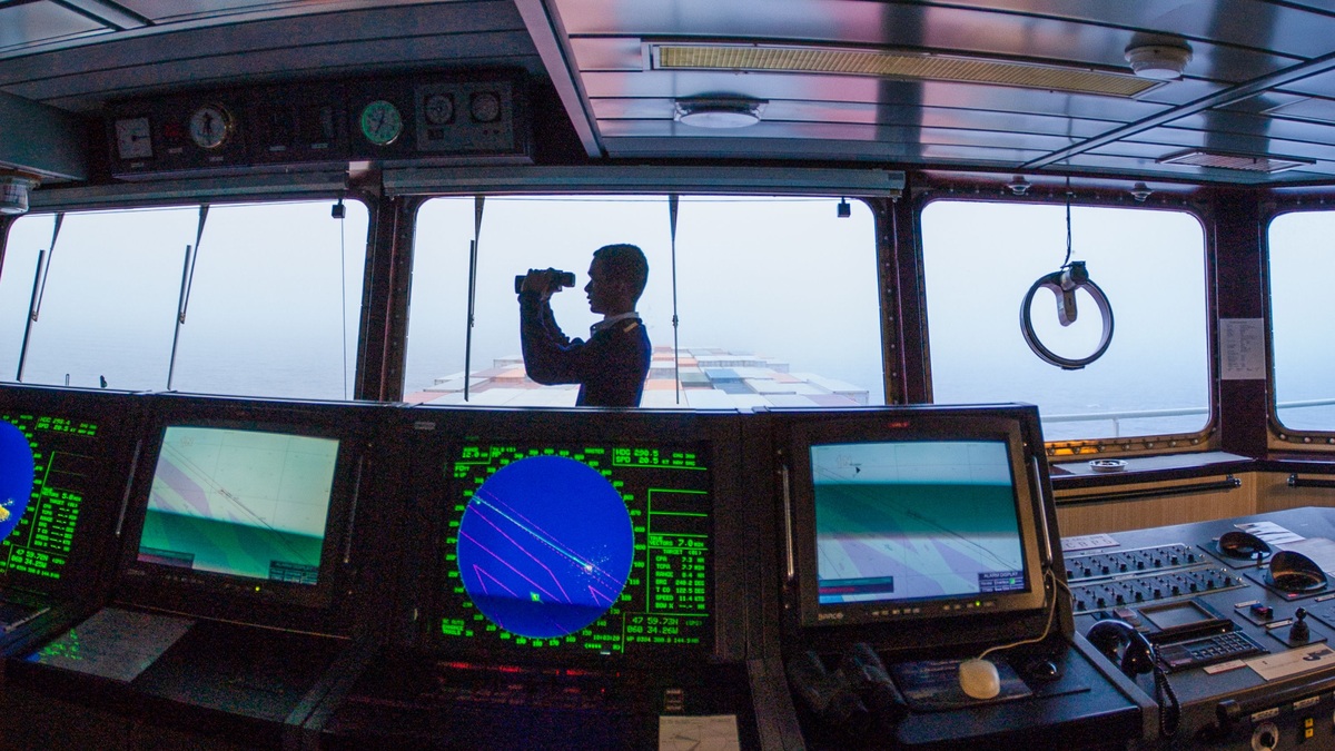 A navigator using binoculars on a ship's bridge