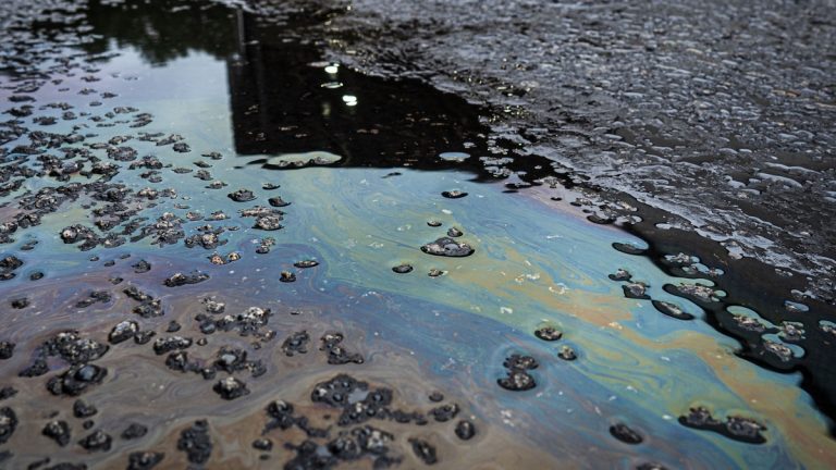 A vivid iridescent oil spill on rough asphalt surface, highlighting environmental contamination